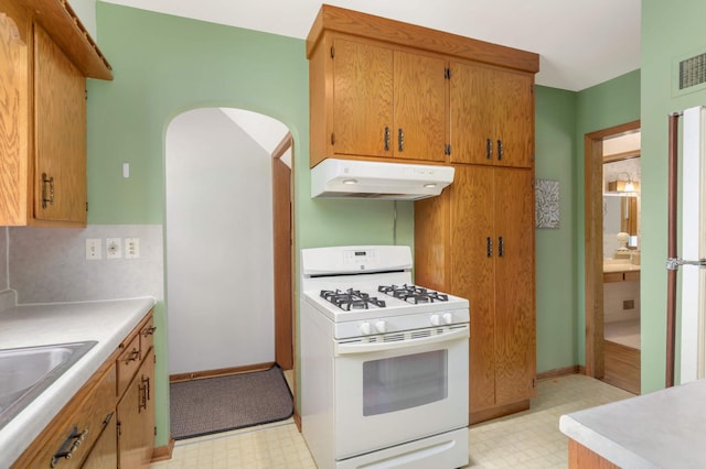 kitchen with arched walkways, a sink, white range with gas cooktop, light floors, and under cabinet range hood