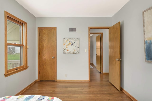 bedroom with baseboards, visible vents, and wood finished floors