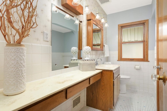 bathroom featuring vanity, toilet, tile patterned floors, a wainscoted wall, and tile walls