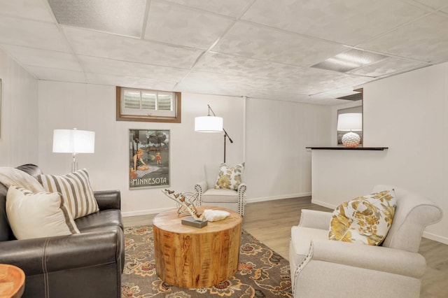 living room featuring baseboards, a drop ceiling, and wood finished floors