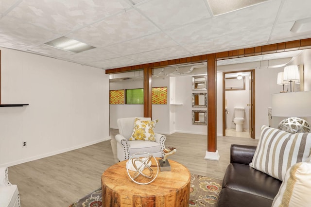 living area with baseboards, a drop ceiling, and wood finished floors