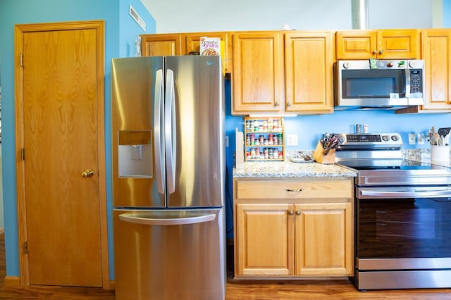 kitchen featuring light stone counters, wood finished floors, light brown cabinets, and stainless steel appliances