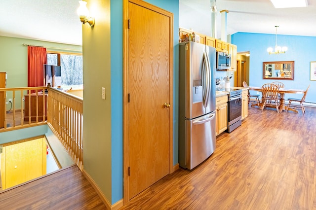 kitchen featuring vaulted ceiling, an inviting chandelier, stainless steel appliances, and light wood finished floors