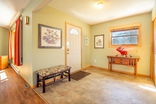 foyer entrance with baseboards, a baseboard radiator, a textured ceiling, and visible vents