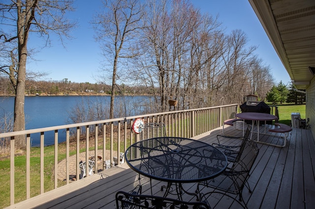 wooden deck featuring outdoor dining space, a water view, and a yard