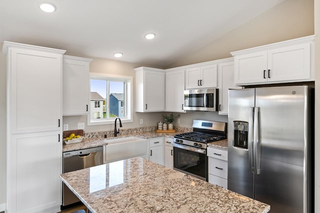 kitchen featuring lofted ceiling, white cabinets, light stone counters, a sink, and appliances with stainless steel finishes