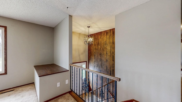 hall with an upstairs landing, carpet flooring, a chandelier, a textured ceiling, and baseboards