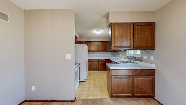 kitchen featuring white appliances, a sink, light countertops, a peninsula, and brown cabinetry