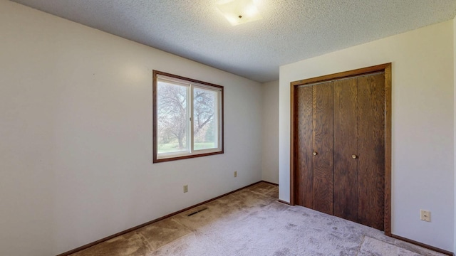 unfurnished bedroom with carpet flooring, a closet, a textured ceiling, and baseboards