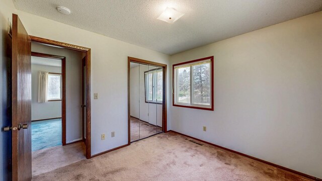 unfurnished bedroom with multiple windows, light colored carpet, baseboards, and a textured ceiling