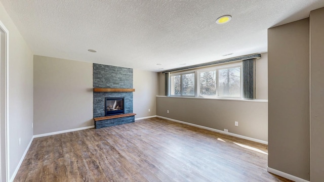unfurnished living room with a textured ceiling, wood finished floors, a fireplace, and baseboards