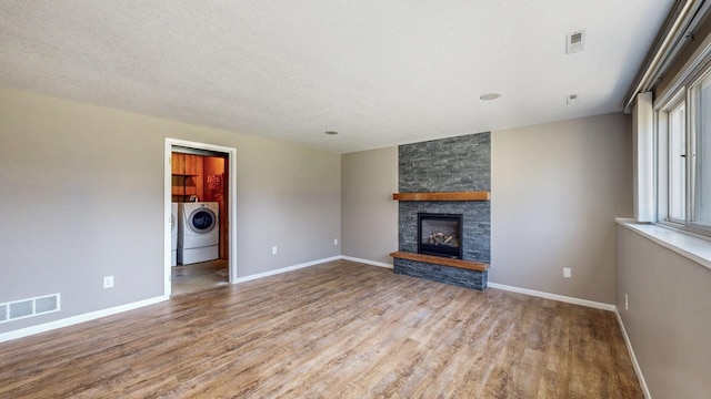 unfurnished living room featuring wood finished floors, washer and dryer, a stone fireplace, and baseboards