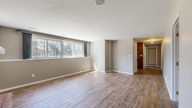 empty room with a textured ceiling, wood finished floors, and baseboards