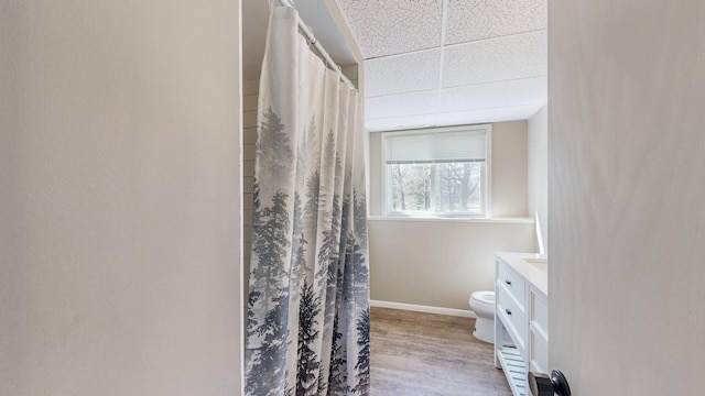 bathroom featuring toilet, a drop ceiling, baseboards, wood finished floors, and vanity