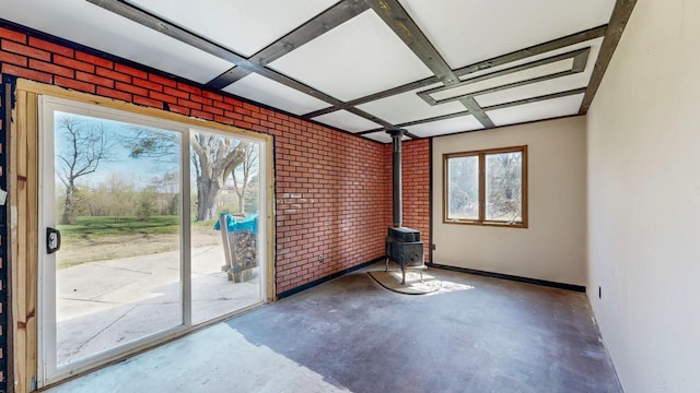 spare room featuring a wood stove, concrete flooring, brick wall, and baseboards