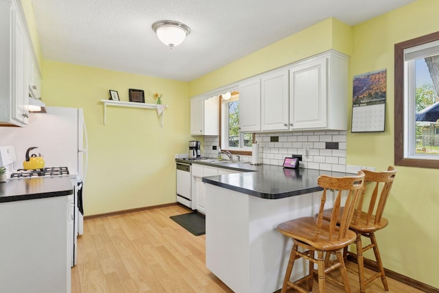 kitchen with a peninsula, white cabinetry, dark countertops, backsplash, and a kitchen bar