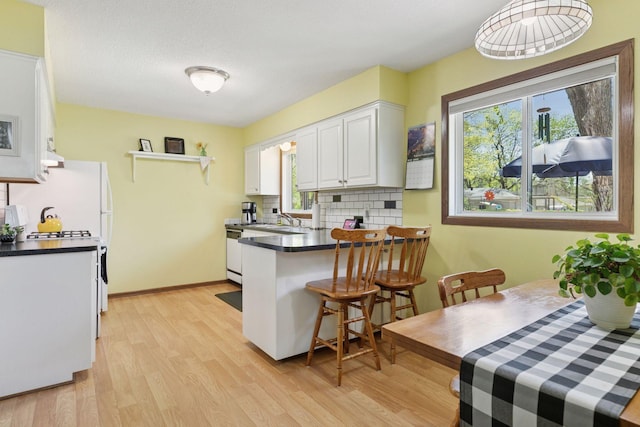 kitchen featuring dark countertops, decorative backsplash, white cabinets, light wood-type flooring, and a sink