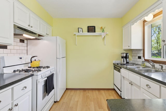 kitchen with white appliances, under cabinet range hood, a sink, dark countertops, and white cabinets