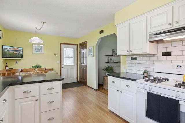 kitchen featuring white gas stove, decorative backsplash, light wood-type flooring, under cabinet range hood, and white cabinets
