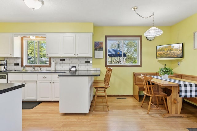 kitchen featuring white cabinets, backsplash, dark countertops, light wood-type flooring, and plenty of natural light