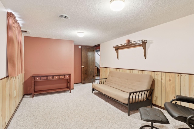 sitting room featuring wood walls, a textured ceiling, carpet, and wainscoting