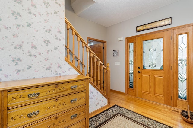 entrance foyer featuring light wood-style flooring, stairs, a textured ceiling, baseboards, and wallpapered walls