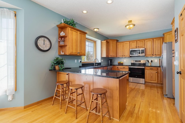 kitchen featuring stainless steel appliances, a peninsula, light wood-style flooring, recessed lighting, and dark countertops