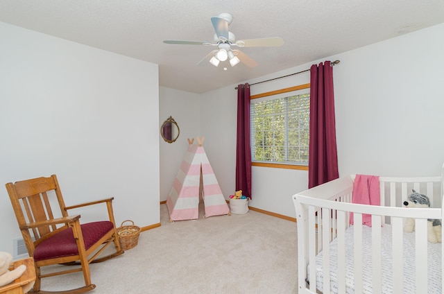 carpeted bedroom featuring baseboards, a nursery area, a ceiling fan, and a textured ceiling