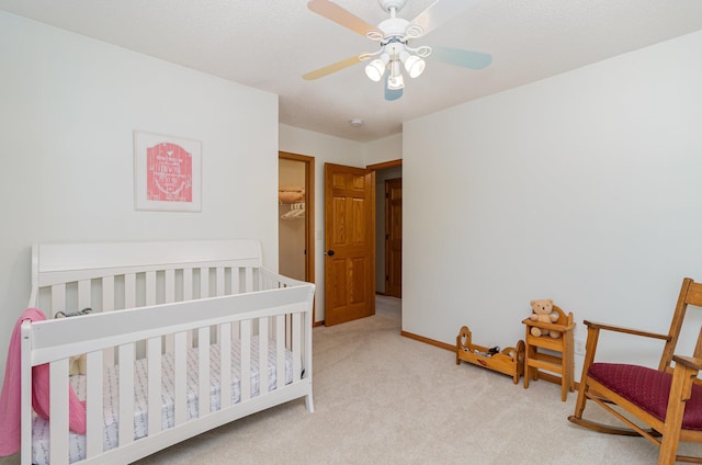 bedroom with carpet floors, a ceiling fan, baseboards, and a crib