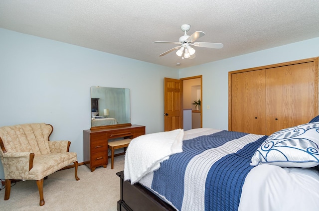 bedroom with light carpet, a closet, a ceiling fan, and a textured ceiling