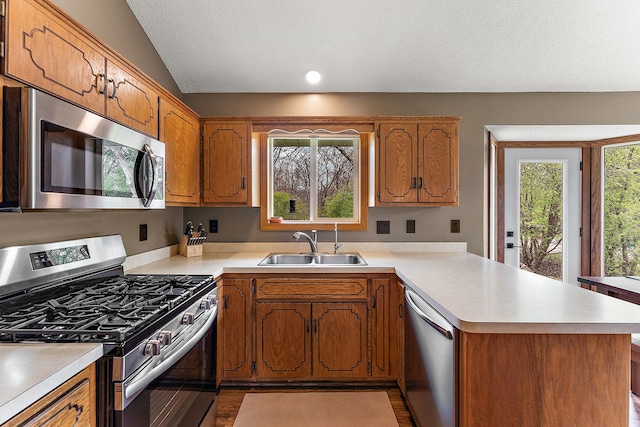 kitchen featuring brown cabinetry, appliances with stainless steel finishes, a sink, light countertops, and a peninsula