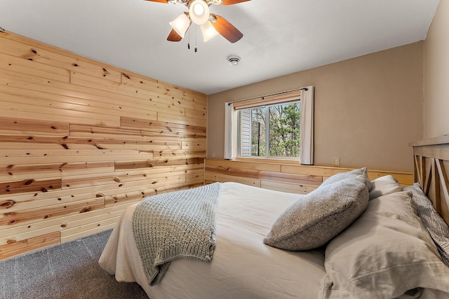 carpeted bedroom featuring wooden walls and a ceiling fan