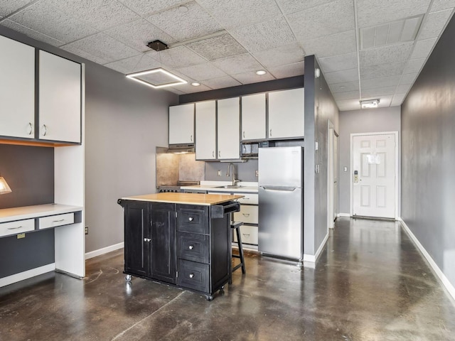 kitchen featuring finished concrete flooring, a sink, baseboards, freestanding refrigerator, and dark cabinetry