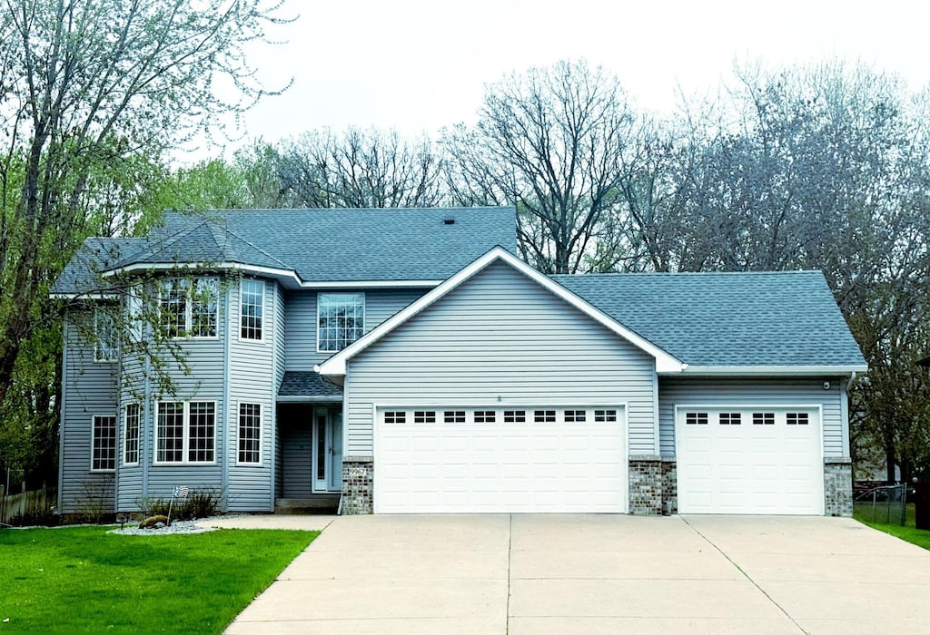 traditional home featuring concrete driveway, a front lawn, roof with shingles, and a garage