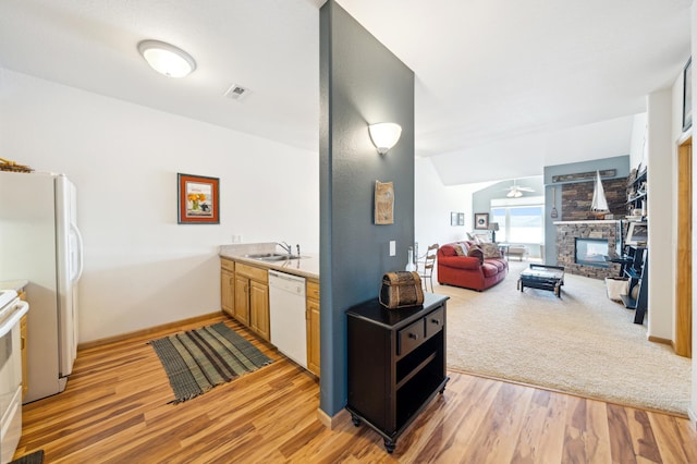 kitchen with white appliances, a fireplace, light wood finished floors, a sink, and baseboards