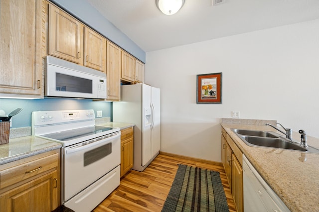 kitchen featuring white appliances, a sink, light wood finished floors, light brown cabinetry, and baseboards