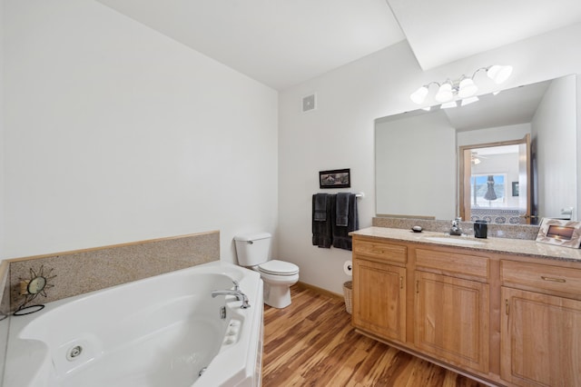 bathroom featuring toilet, a jetted tub, wood finished floors, and vanity