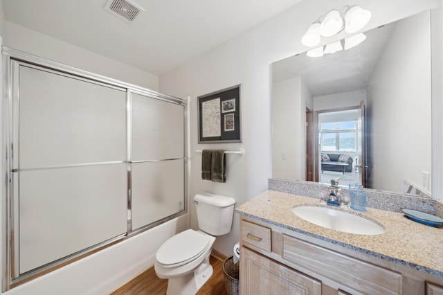 bathroom with wood finished floors, toilet, vanity, and shower / bath combination with glass door