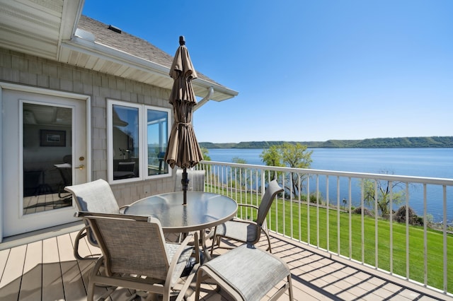 wooden terrace featuring a water view, a lawn, and outdoor dining space