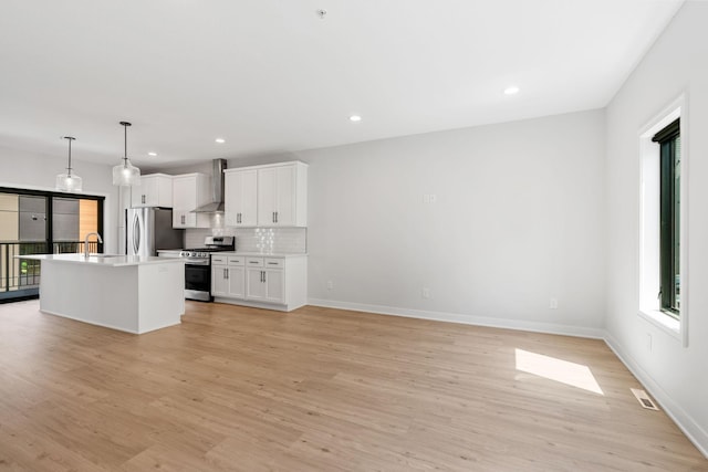 kitchen with wall chimney range hood, appliances with stainless steel finishes, plenty of natural light, and light wood-type flooring