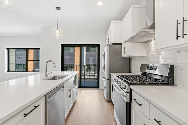 kitchen featuring wall chimney range hood, appliances with stainless steel finishes, tasteful backsplash, a sink, and light wood-style floors