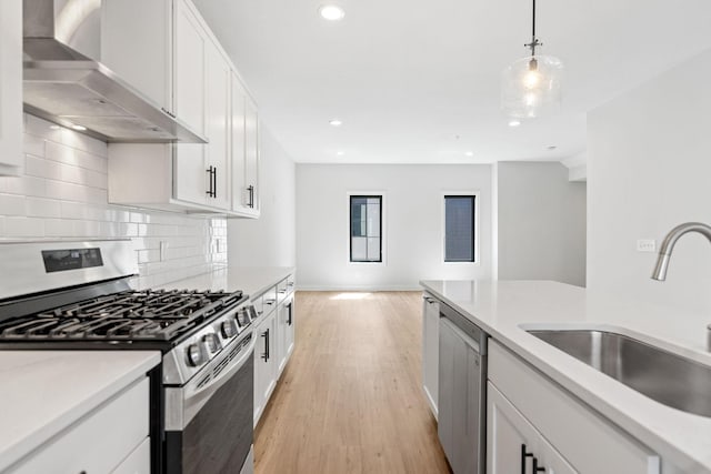 kitchen featuring decorative backsplash, appliances with stainless steel finishes, a sink, recessed lighting, and wall chimney exhaust hood