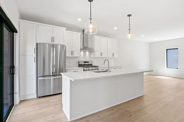kitchen with wall chimney range hood, appliances with stainless steel finishes, a sink, light wood-style floors, and recessed lighting