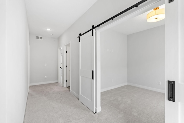 hall featuring visible vents, a barn door, baseboards, and carpet flooring