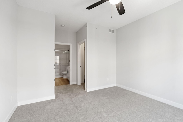 unfurnished bedroom featuring ceiling fan, carpet, baseboards, ensuite bathroom, and visible vents
