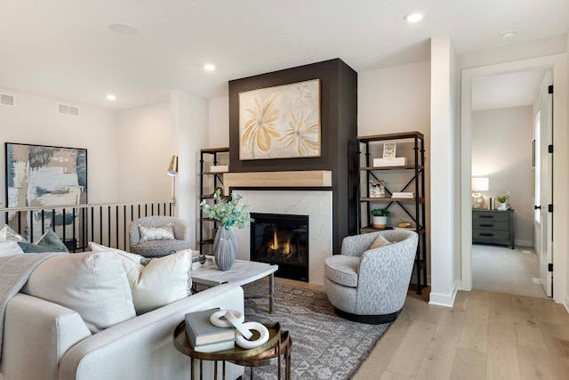 living area featuring recessed lighting, visible vents, a high end fireplace, and light wood-type flooring