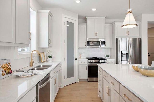 kitchen featuring a sink, stainless steel appliances, white cabinetry, light wood-type flooring, and pendant lighting
