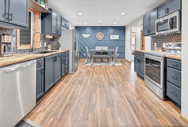 kitchen featuring butcher block countertops, backsplash, a sink, stainless steel appliances, and light wood-style flooring