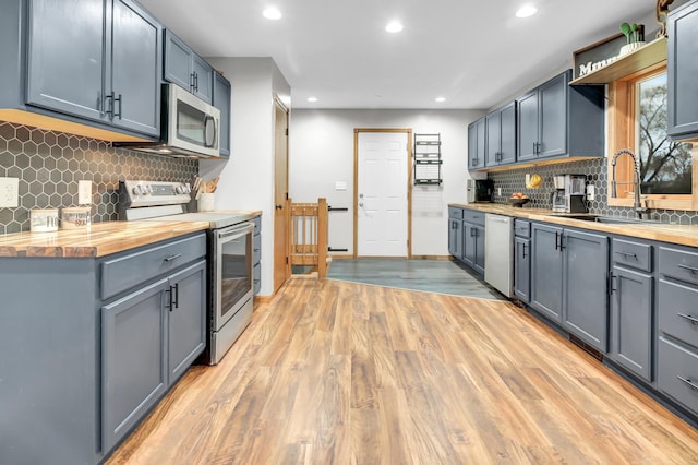 kitchen featuring stainless steel appliances, butcher block countertops, a sink, and light wood-type flooring