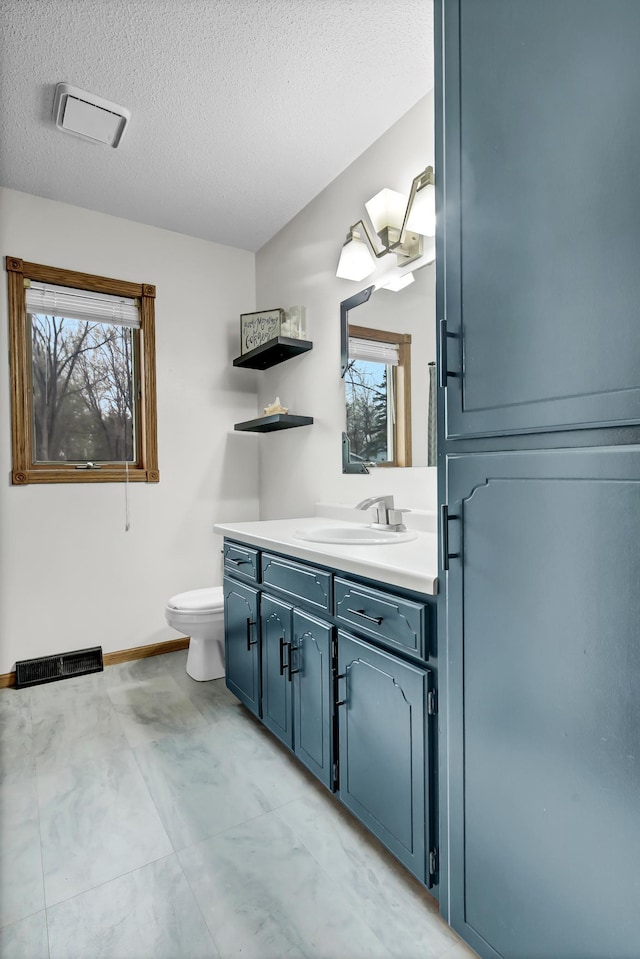 bathroom with visible vents, vanity, toilet, baseboards, and a textured ceiling